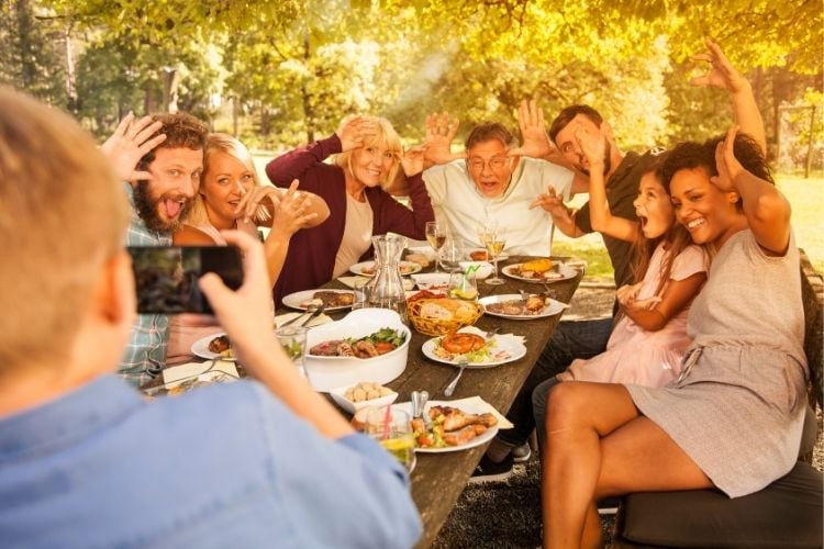 Foto de família com homens e mulheres de diferentes tons de pele, reunida ao redor de mesa com alimentos