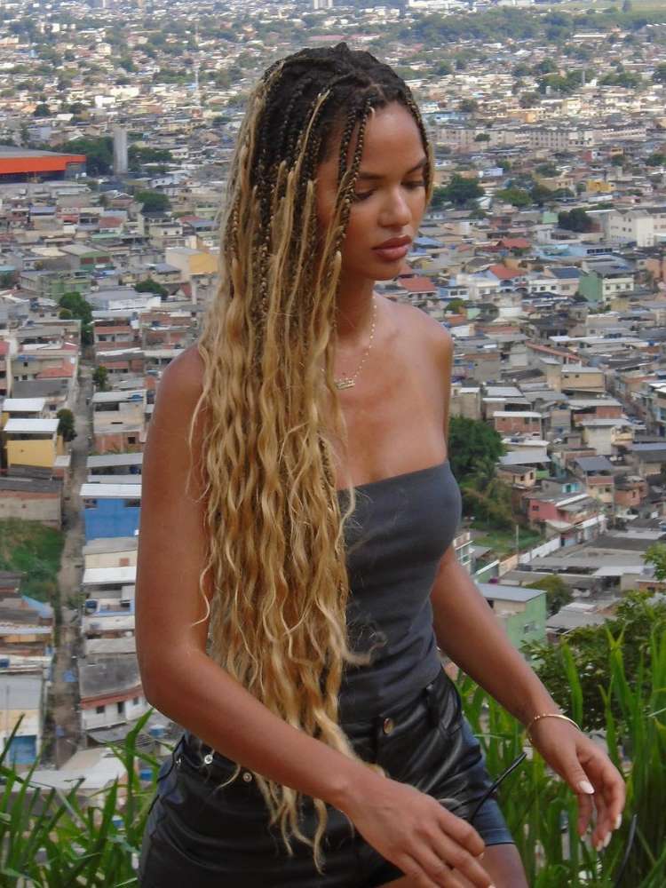 Juliana Nalu em foto com cidade ao fundo, usando cropped cinza sem alças, shorts preto e gypsy braids