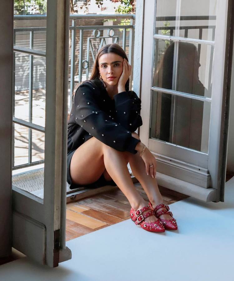 Mulher sentada na beira de uma porta, com sapatilha vermelha bailarina, da marca de roupa Vinci Shoes do Rio Grande do Sul