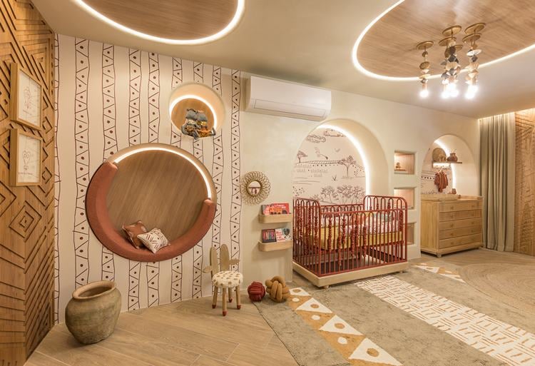 A imagem mostra um quarto infantil bem iluminado com decoração temática tribal. Inclui uma cama com grade, tapetes geométricos, espelhos redondos e iluminação embutida no teto. As paredes têm desenhos de flechas e tendas.