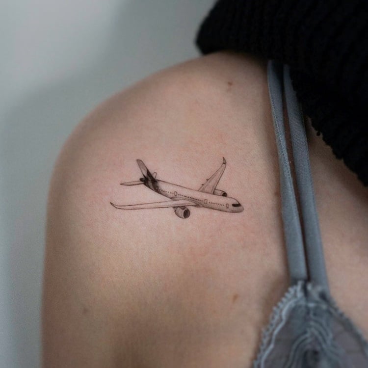 Tatuagem de avião preto e branco em ombro de mulher