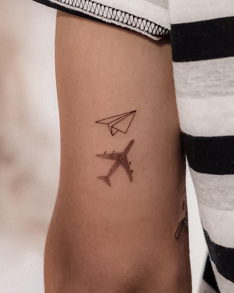 Tatuagem de avião de papel com sombra de avião de verdade em braço de mulher