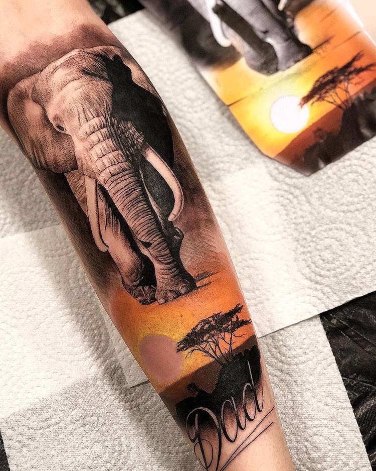 Tatuagem de viagem inspirada na África, com elefante e por do sol em paisagem em braço