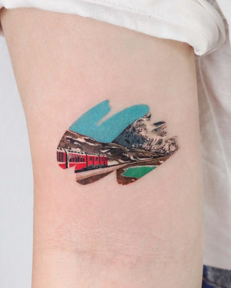 Tatuagem de tinta com trem andando em meio aos alpes 