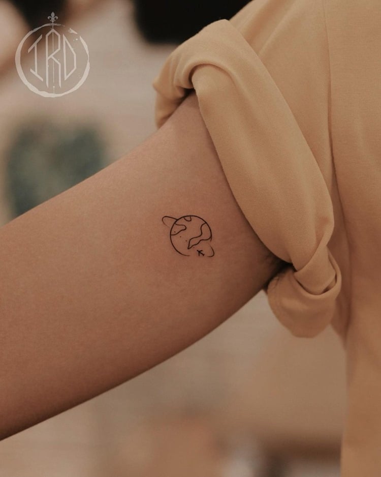 Tatuagem minimalista de globo com avião em volta em braço de mulher