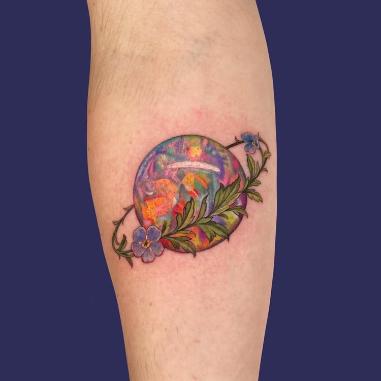 Tatuagem de mundo colorido com arco floral em volta