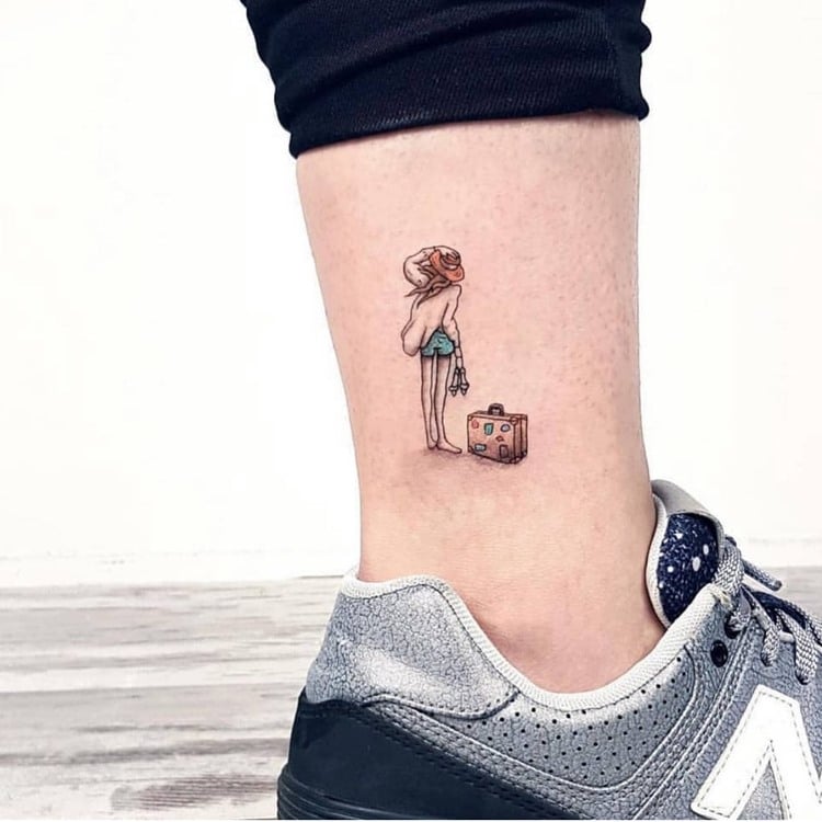 tattoo de garota com uma mala cheia de adesivos na canela de uma pessoa