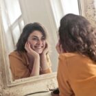 Foto de mulher morena de camisa amarela olhando a autoimagem no espelho