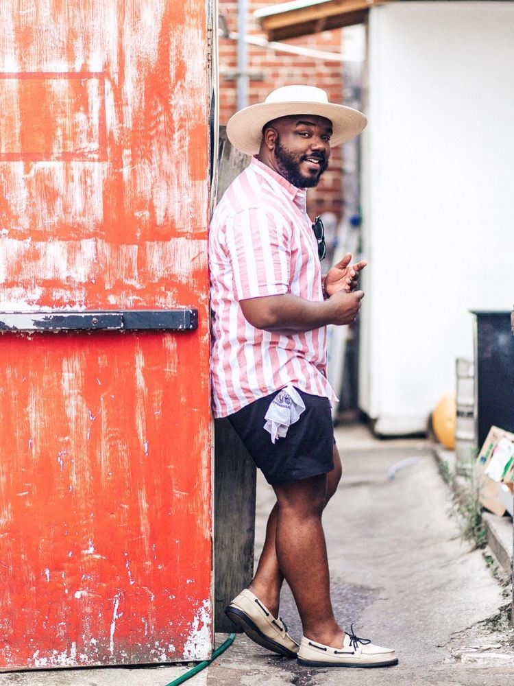 Homem com tipo de corpo oval usando camisa listrada rosa e branca com shorts azul marinho