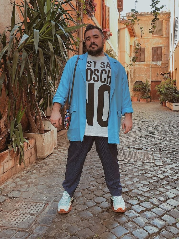 Homem usando camiseta branca e preta com blazer azul e calça jeans escura