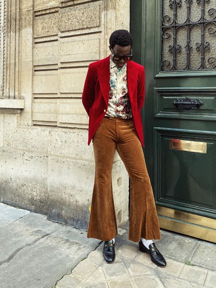 Homem com formato de corpo triângulo invertido usando camisa florida, blazer vermelho e calça marrom