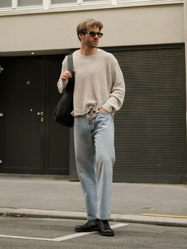 Homem com tipo de corpo triângulo usando suéter oversized areia com gola canoa e calça jeans reta