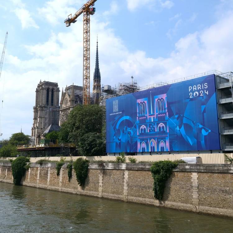 Foto de telão azul com desenho da Notre Dame, logo das Olimpíadas 2024 e rio Sena