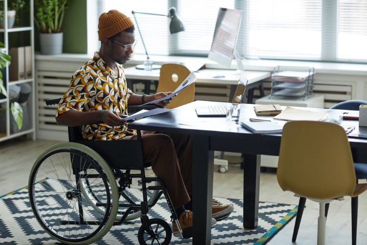 Rapaz deficiente em cadeira de rodas, trabalhando em uma mesa grande em um escritório moderno