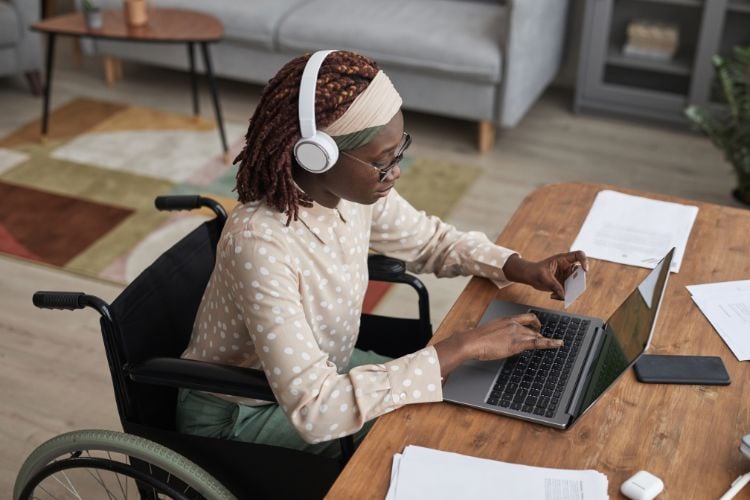 Mulher em cadeira de rodas trabalhando em mesa no seu notebook