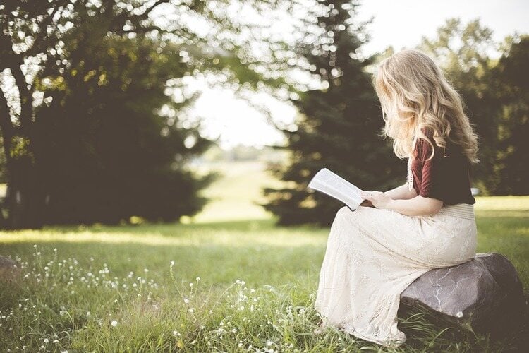 Mulher loira sentada na natureza lendo um livro