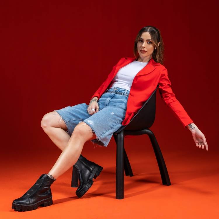 mulher sentada na cadeira usando botas chelsea, bermuda, blazer vermelho
