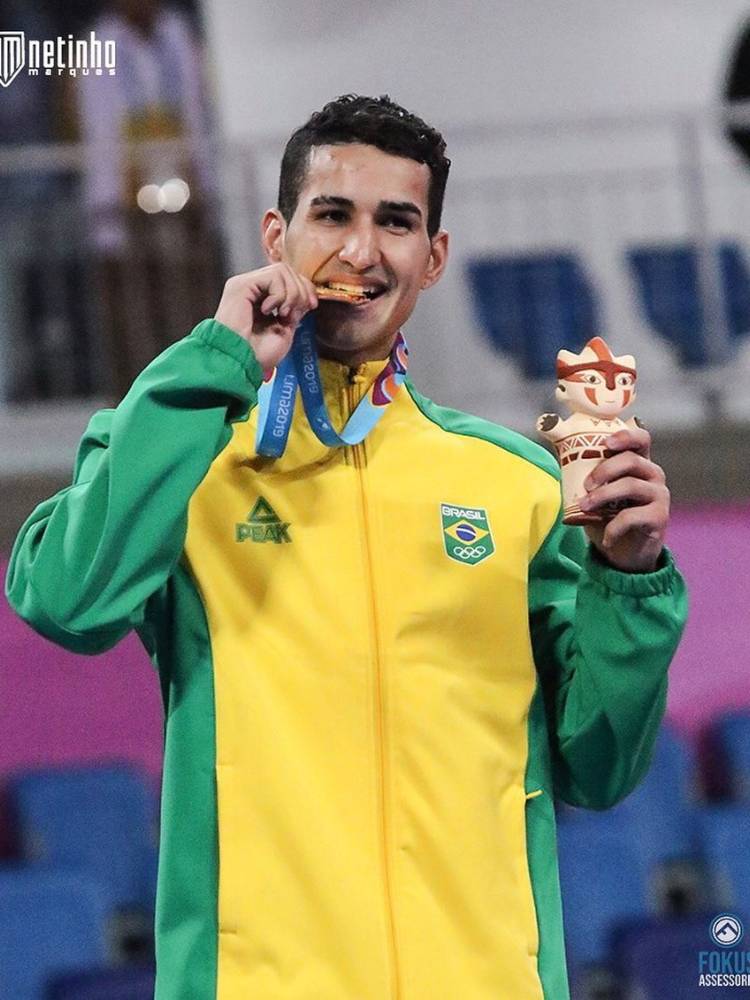 Henrique Marques usando casaco do Brasil e mordendo medalha dos Jogos Pan-Americanos 2023
