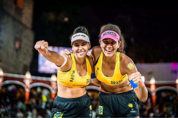 Duda e Ana Patrícia com uniforme brasileiro de vôlei de praia comemorando em quadra