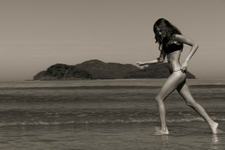 Foto em preto e branco de praia e mulher correndo de biquíni