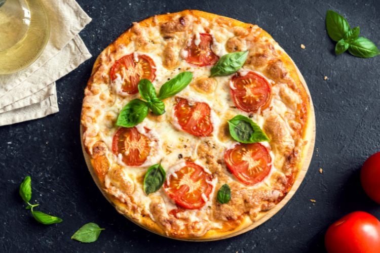Foto de pizza de mussarela com tomate e manjericão sobre mesa azul