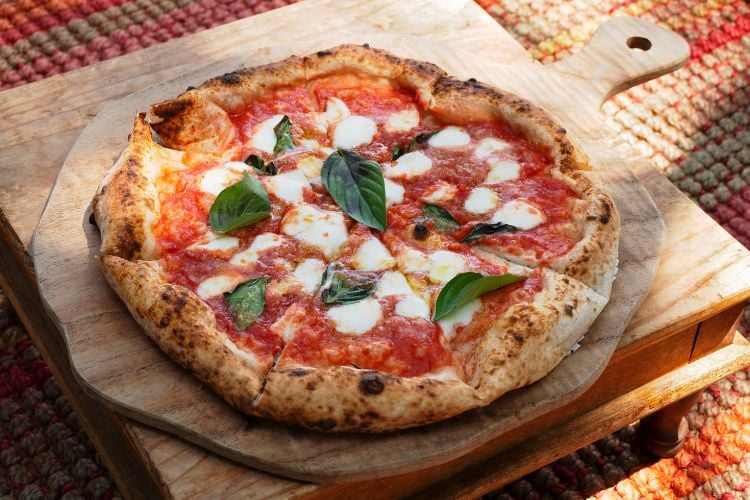 Foto de pizza com molho de tomate, mussarela de búfala e manjericão sobre tábua de madeira