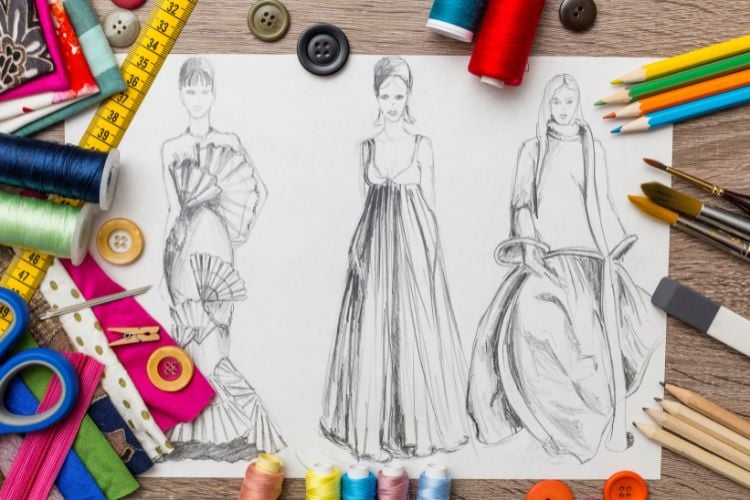 3 vestidos de moda desenhados em papel com diversos itens de desenho de estilista ao redor