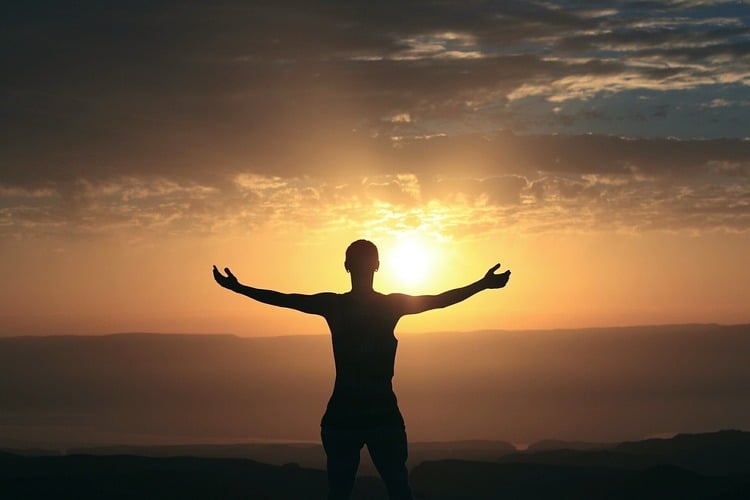 Pessoa se conectando com a espiritualidade no meio da natureza, de braços abertos em frente ao por do sol