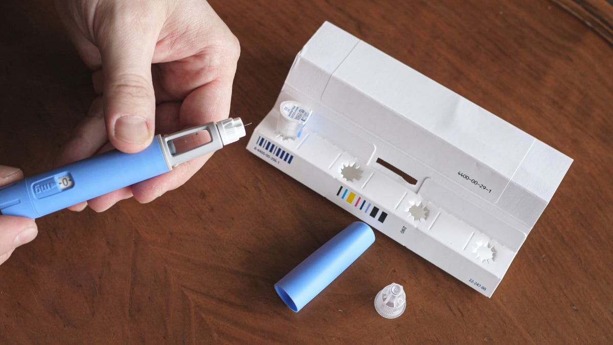 Foto de pessoa de pele clara manuseando medicamento em caneta, ao lado de tampa e embalagem