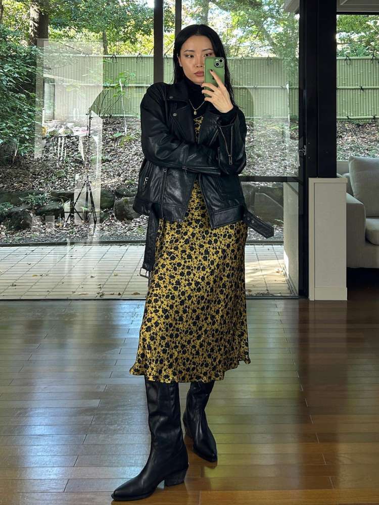 Mulher asiática usando blusa preta por debaixo de slipdress, jaqueta de couro e bota preta cano alto