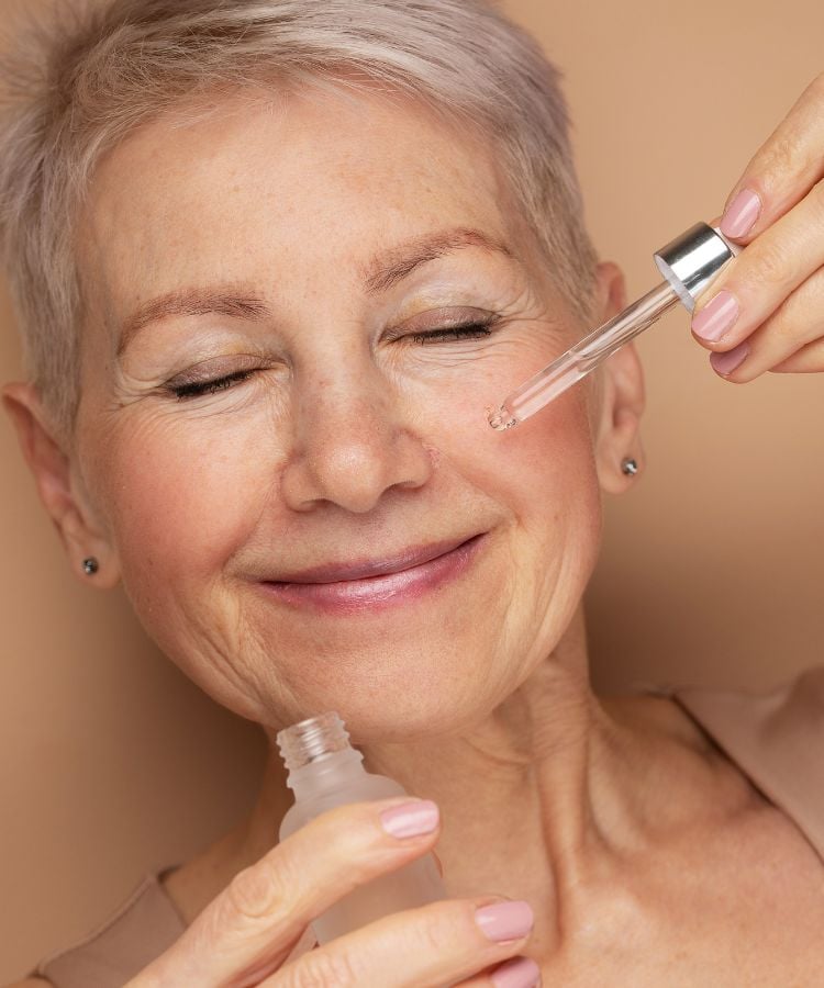Mulher idosa sorrindo aplicando sérum com retinol no rosto