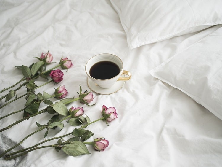 Lençóis brancos com uma xícara de café e rosas vermelhas do lado