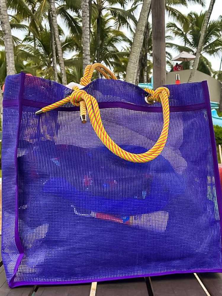 Bolsa azul escura com itens de praia dentro e alça amarela
