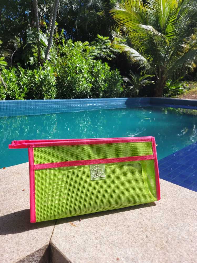 Necessaire feita de materiais reciclados nas cores verde e rosa, em beirada de piscina