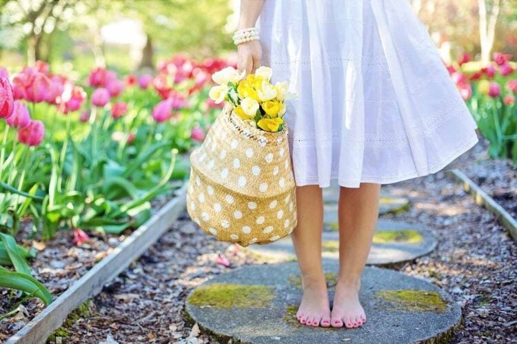 Mulher descalça com uma cesta de tulipas no meio da natureza