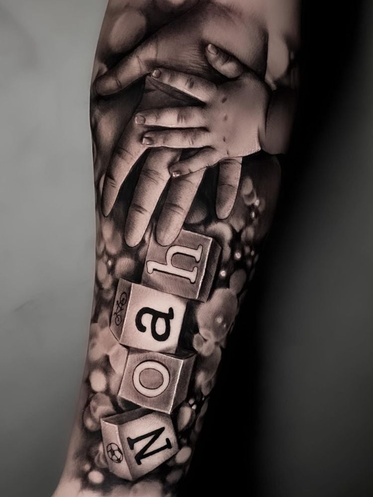 Tatuagem realista de mão grande e mão pequena, com nome Noah escrito soletrado em cubos