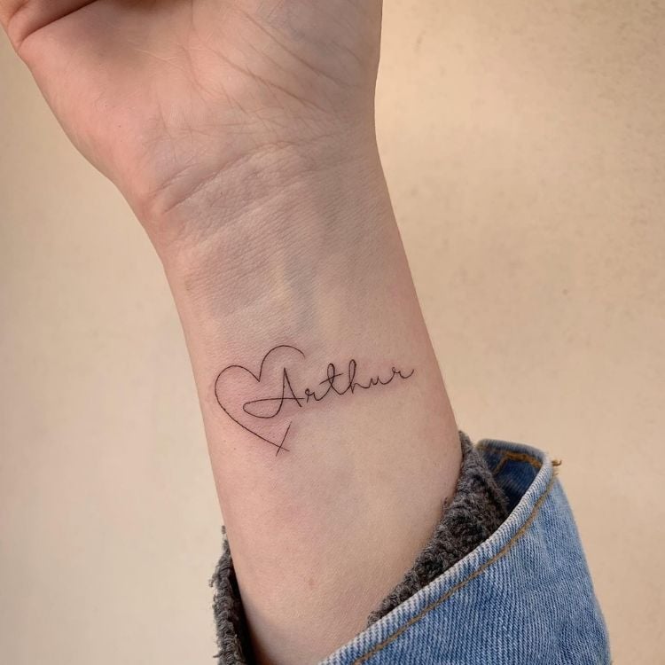 Foto de pulso de pessoa de pele clara com tatuagem de coração e nome Arthur
