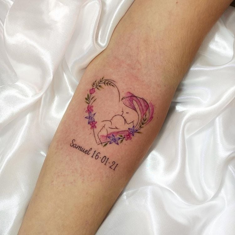 Foto de tatuagem em formato de coração com flores coloridas, desenho de mãe beijando cabeça de neném e nome com data de nascimento