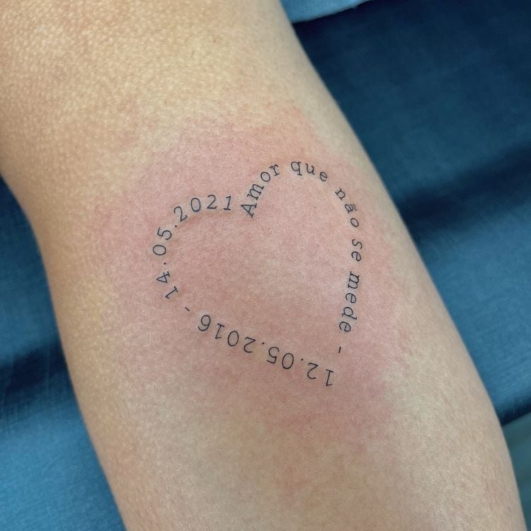 Foto de tatuagem em formato de coração com frase "amor que não se mede" e datas
