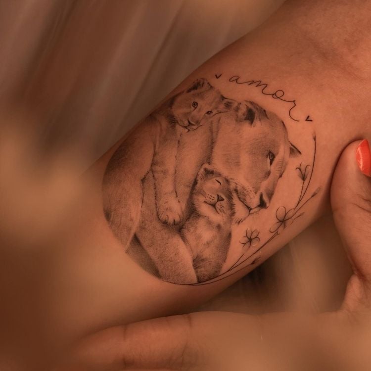 Foto de braço de mulher com tatuagem realista de leoa com filhotes e palavra "amor"