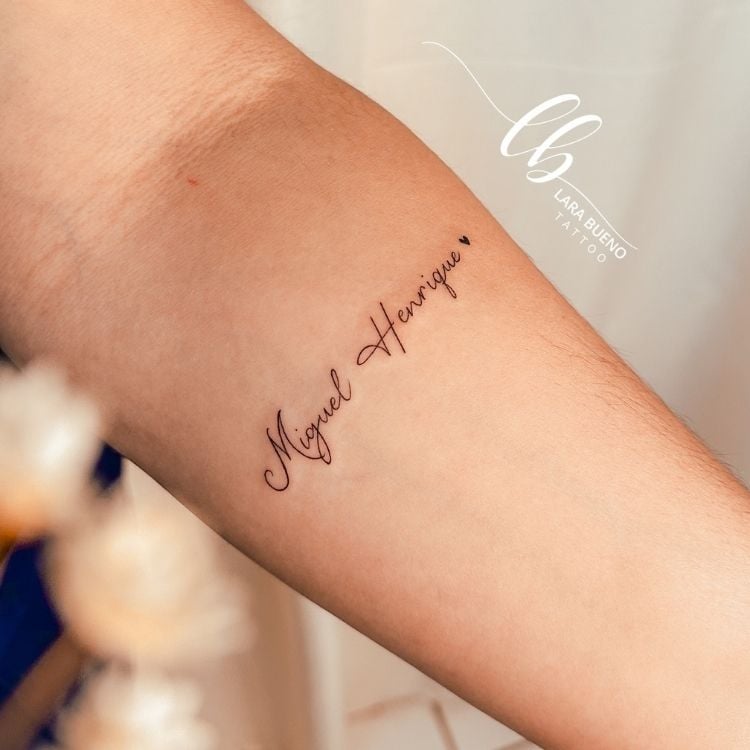 Braço de pessoa de pele clara com tatuagem escrito "Miguel Henrique"