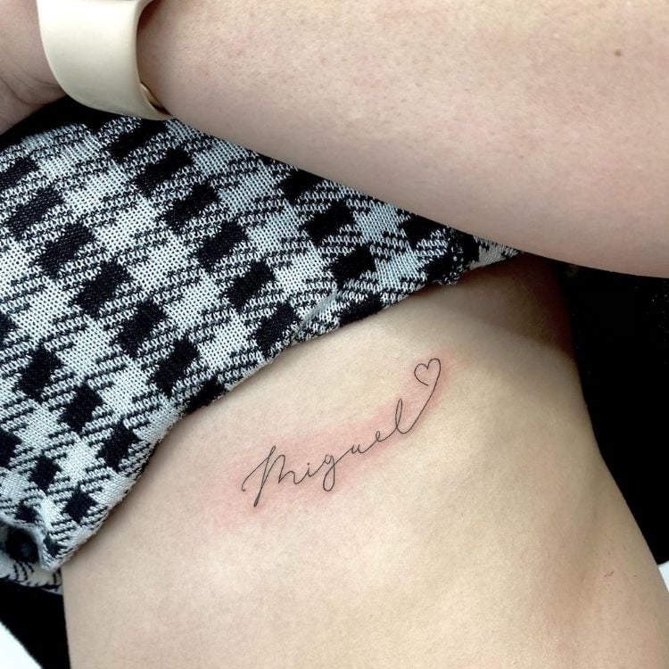 Costela de pessoa de pele clara com tatuagem escrito "Miguel" e um coração