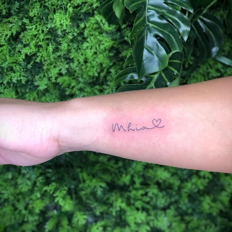 Pulso de pessoa de pele clara com tatuagem escrito "Mhia" 
