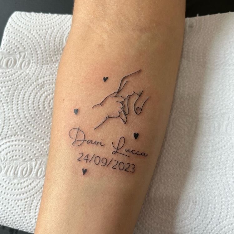 Foto de tatuagem de mão de bebê segurando dedo de adulto, nome "Davi Lucca" e data de nascimento