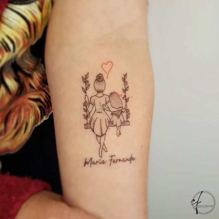 Foto de tatuagem de mãe e filha em balanço, com nome "Maria Fernanda"