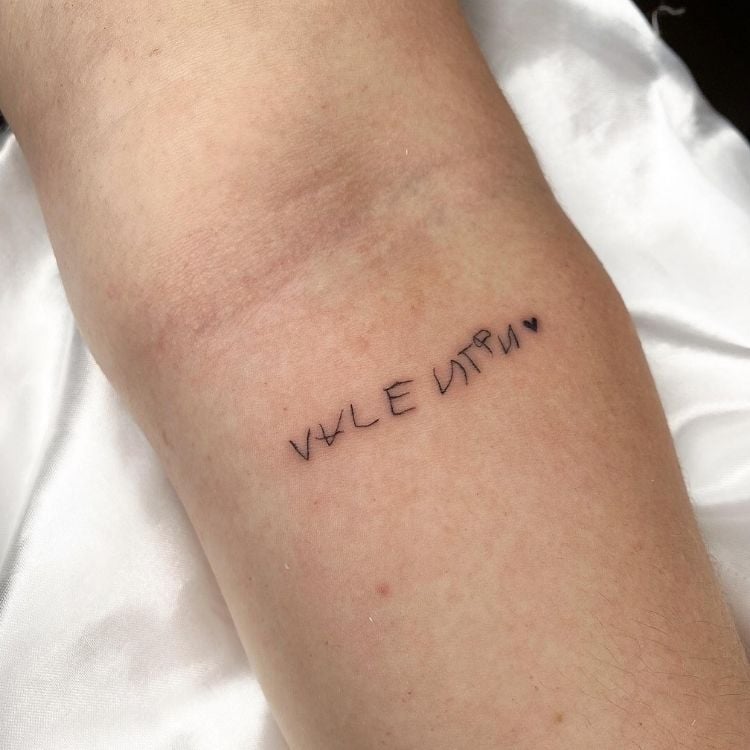 Pessoa de pele clara com tatuagem escrito "Valentin" com a letra da criança no braço