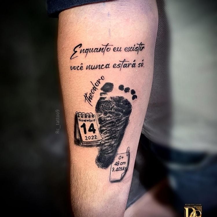 Tatuagem de impressão do pé de um bebê, com informações de nascimento, nome e frase "enquanto eu existir você nunca estará só"