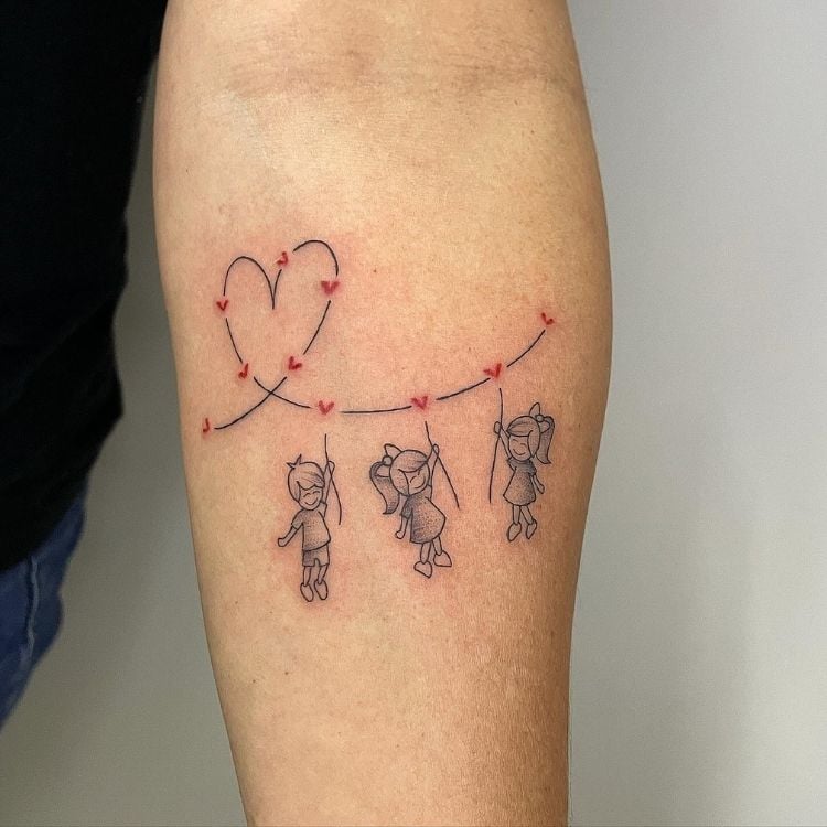Foto de braço de mulher com varal de coração tatuado, com três desenhos de bebês pendurados