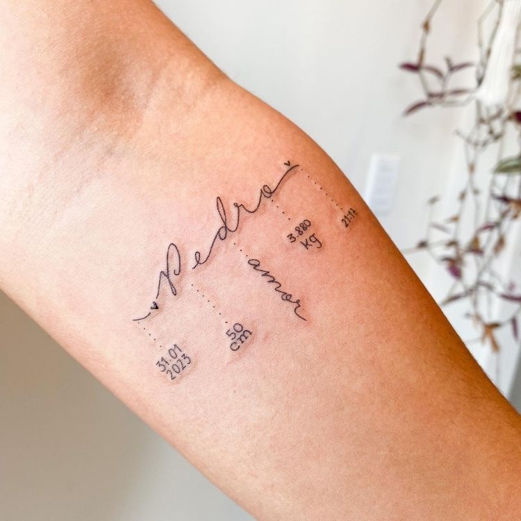 Tatuagem de nome de filho com dados no nascimento em braço de pessoa de pele clara 