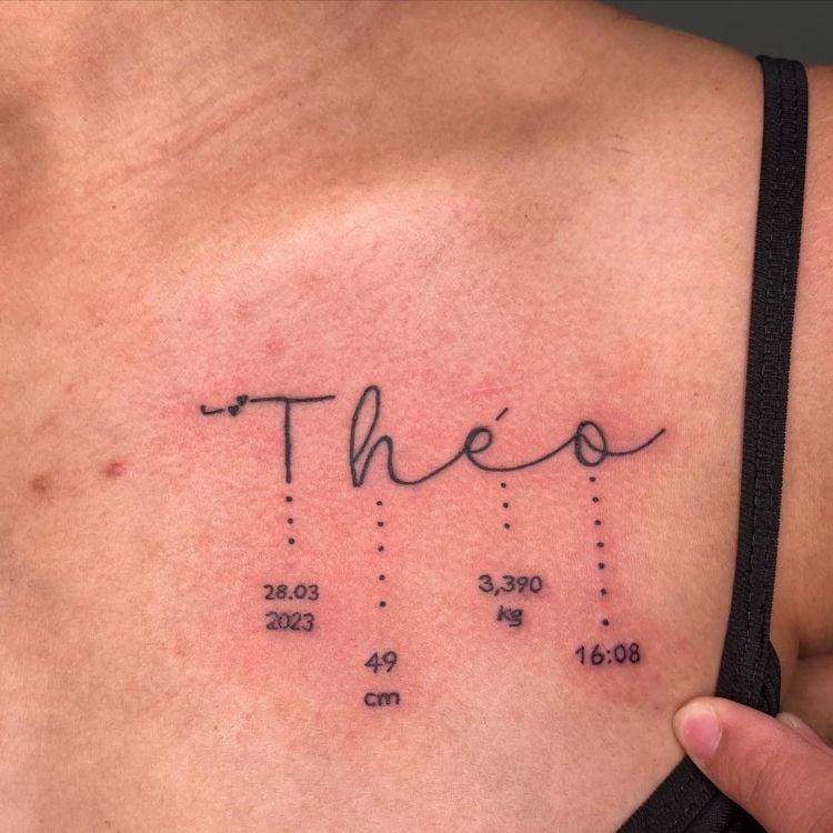 Mulher de pele clara com tatuagem no ombro escrito "Theo" e varal com informações de nascimento do filho 